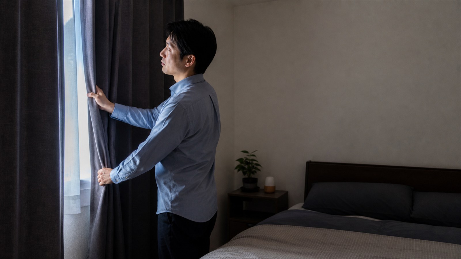 夜勤明けの朝、遮光カーテンを整えて就寝準備をする日本人男性